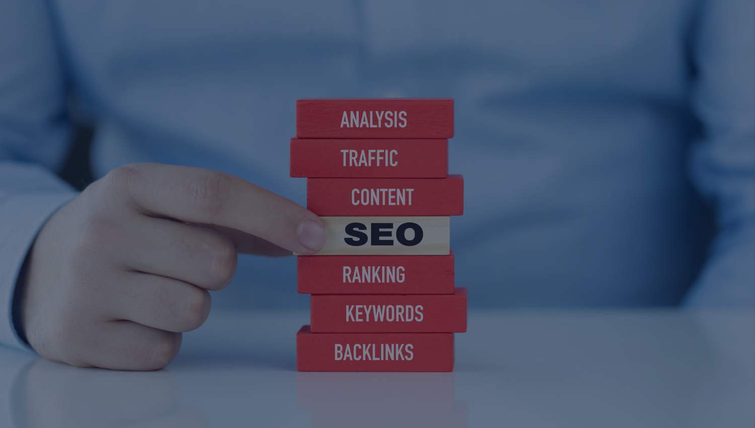 Hand stacking SEO blocks labeled analysis, traffic, content, SEO, ranking, keywords, and backlinks